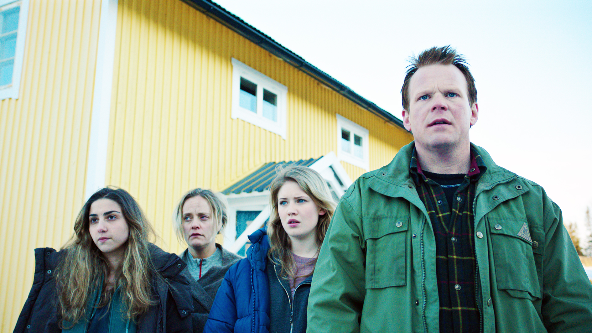 Filmstill aus "Welcome to Norway": Ein Mann und drei Frauen unterschiedlichen Alters in Winterjacken. Hinter ihnen ein gelbes Holzhaus. Sie schauen entsetzt.