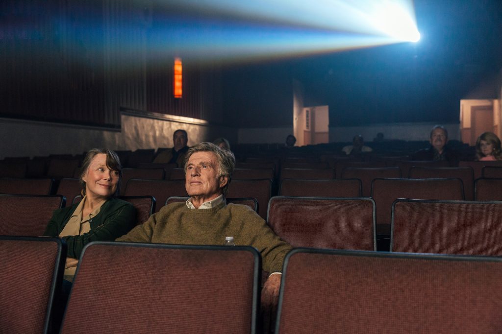 Filmstill aus "Ein Gauner & Gentleman": Ein Mann und eine Frau im Kino, sie lächelt ihn an.