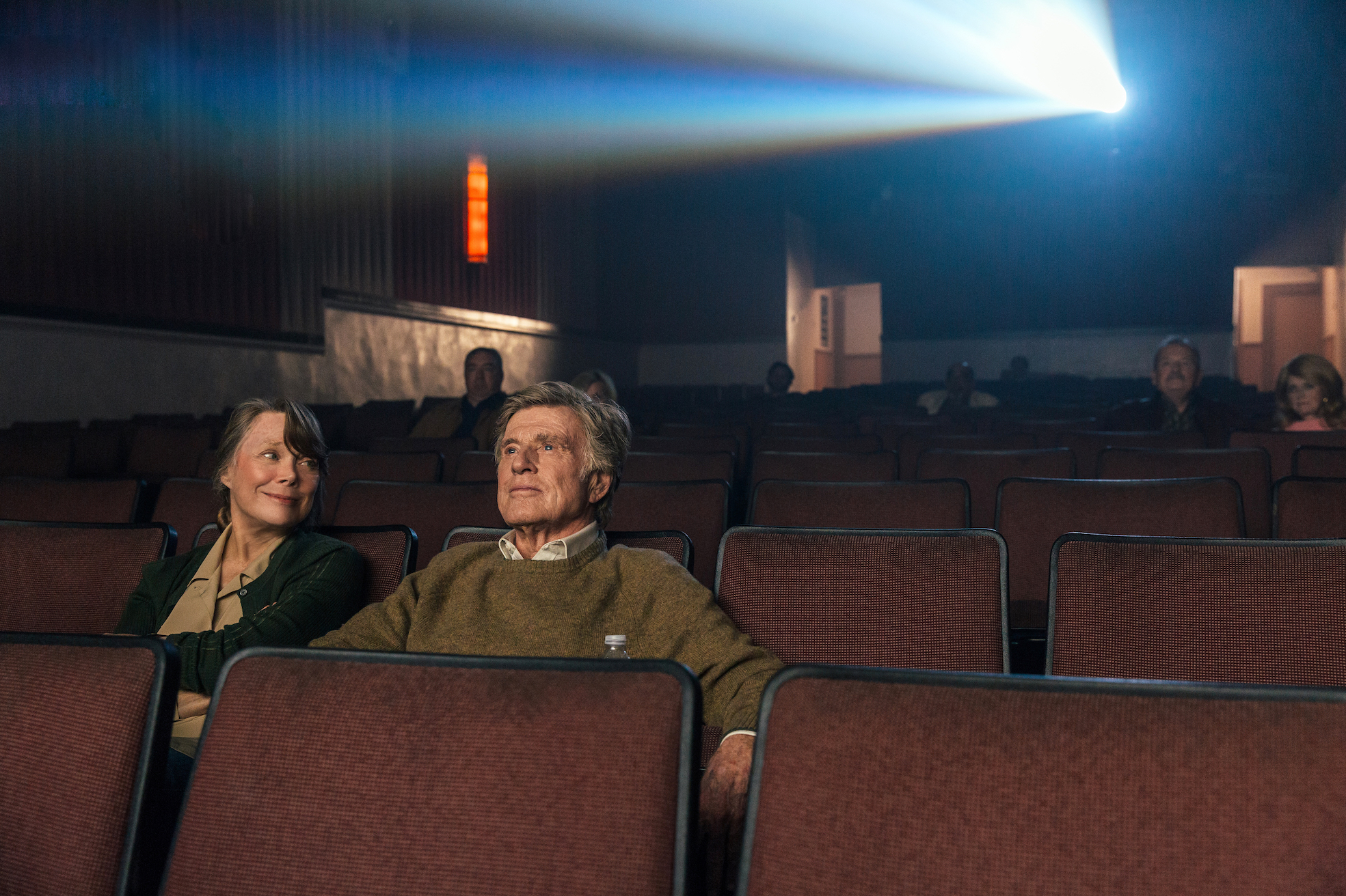 Filmstill aus "Ein Gauner & Gentleman": Ein Mann und eine Frau im Kino, sie lächelt ihn an.