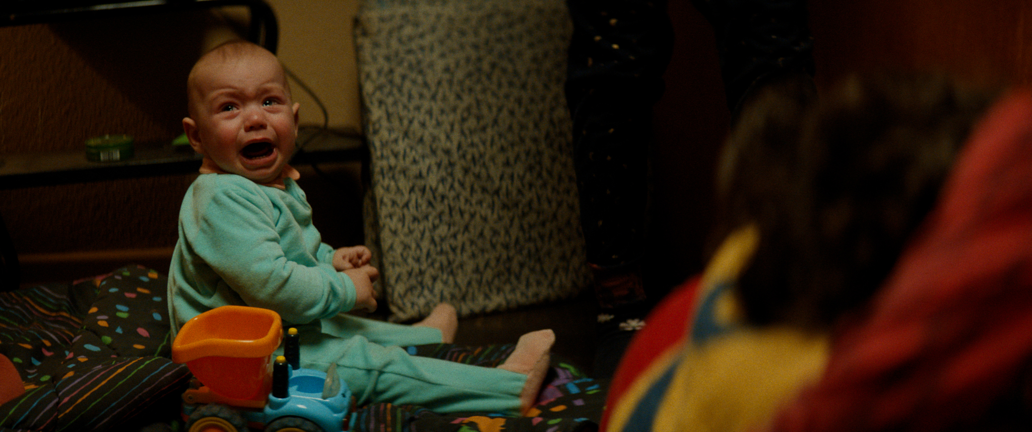 Filmstill aus "Kids Run": Ein schreiendes Baby sitzt auf dem Fußboden einer Wohnung.