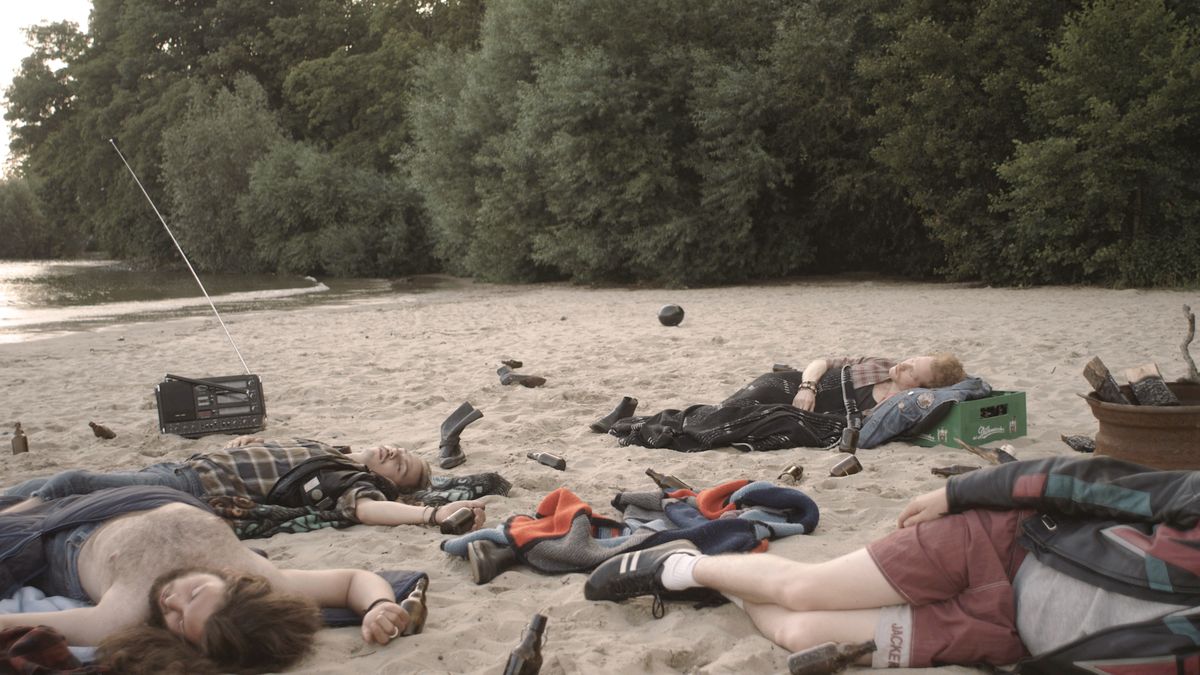 Junge Menschen liegen zwischen Flaschen und Stiefeln schlafend am Strand