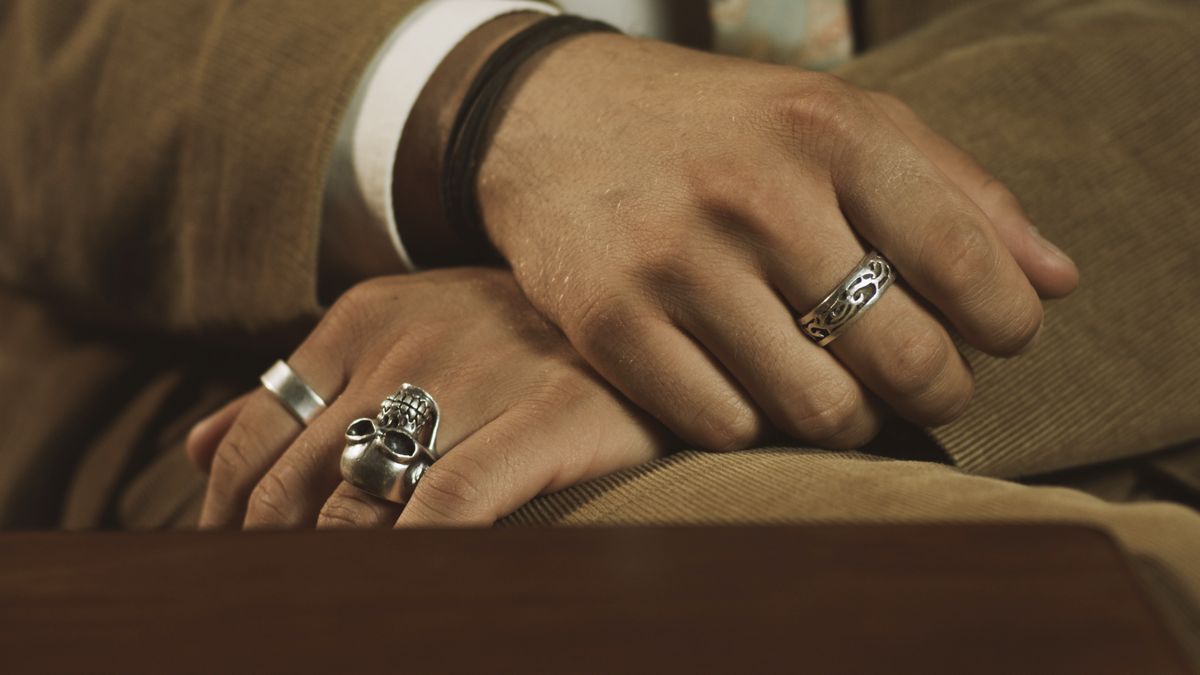 Die Hände eines Mannes mit Ringen an den Fingern. An der linken Hand trägt er einen Totenkopf-Ring.