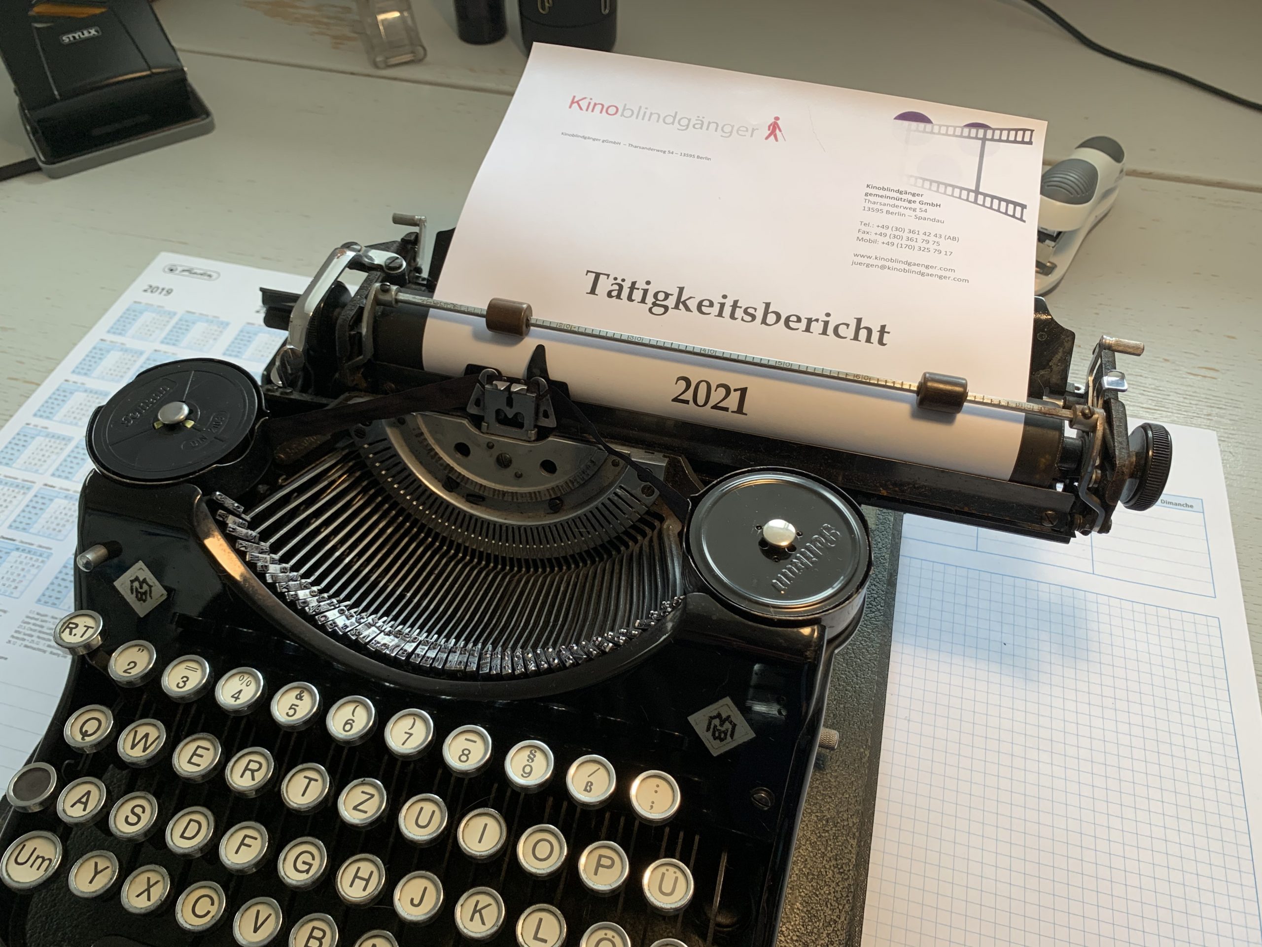 Eine alte schwarze Schreibmaschine mit Typenhebeln. Eingespannt ist ein Bogen mit der Überschrift "Tätigkeitsbericht 2021".