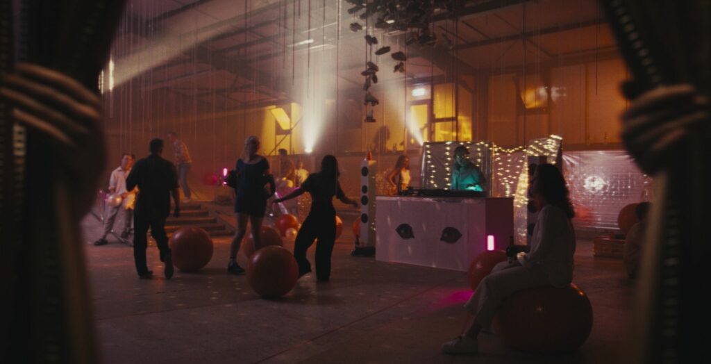 Filmstill "To Cut A Long Story Short​": Tanzende Menschen in einer Diskothek