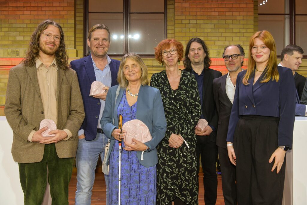 Das Team von Kinoblindgänger bei der Preisverleihung. Auf der Bühne stehen Timo Mehrländer, Sascha Gluth, Barbara Fickert, Susanne Linzer, Ralf Krämer, Yves Kugelmann und Lilly Charlotte Dreesen.